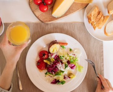 A top-view of a delicious breakfast setting featuring a salad, bread, cheese, tomatoes, and orange juice.