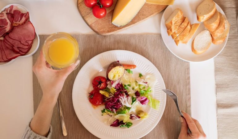 A top-view of a delicious breakfast setting featuring a salad, bread, cheese, tomatoes, and orange juice.